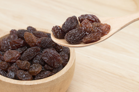 raisins in spoon with raisins in bowl on wooden table.の写真素材