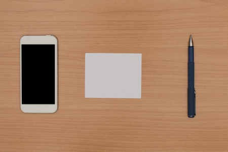 Top view of wooden desk with blank smart phone, pen and paper noteの写真素材