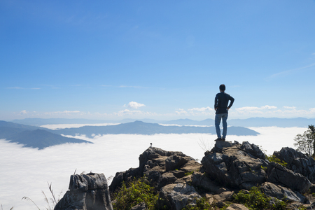 man standing on the cliff and looking at the valley and mountains in the daylightの写真素材