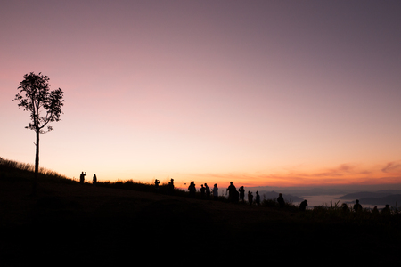 silhouette of people the cliff and looking at the valley and mountains with sunrise in the morningの写真素材