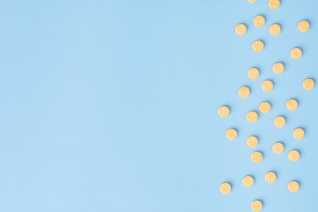 Yellow medical pills on blue background with copy space.