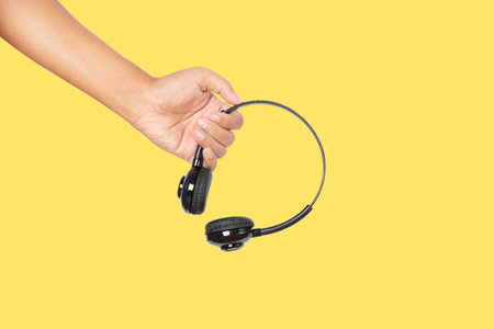 Hand holding headphones isolated on yellow background.の写真素材