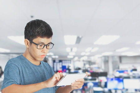 A young man using a tablet and touching screen, working online in office building background.
