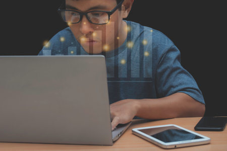 Asian man working at a desk with a computer laptop and tablet and smartphone. Home working ideas table setting is casual, with a concept with a Forex graph.の写真素材