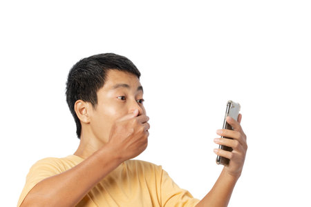 Young asian man shocked and surprised news on smartphone isolated on white backgroundの写真素材