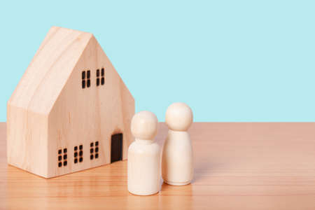 wooden doll couple stands in front of house model on blue background. Family home, Insurance and property investment real estate concept.の写真素材
