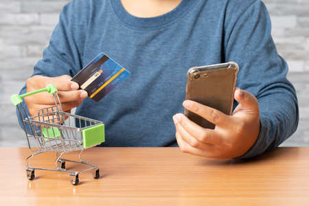 Young man holding credit card with smart phone on desk. Online shopping, e-commerce.