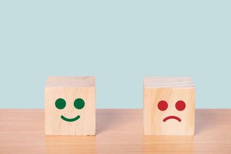 Smiley face and blurred sad face icon on the wood cube, Customer service rating, Satisfaction survey concept.の写真素材