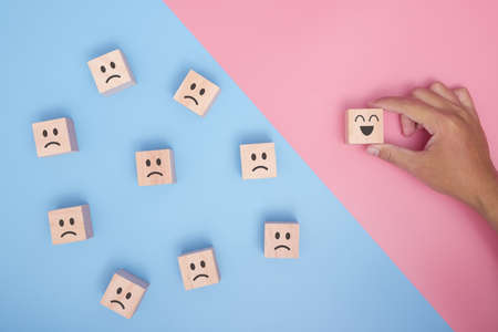 Hand holding wood cube with smiley face icon symbol on blue and pink background. Customer service rating, Satisfaction survey concept.の写真素材