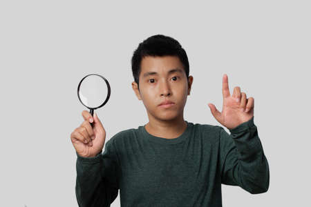 Young man holding magnifying glass and point index finger up with new idea on gray background.の写真素材