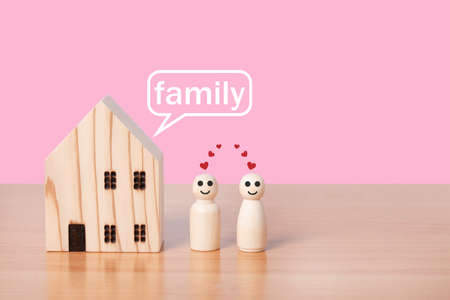 wooden doll couple stands in front of house model on pink background. Family home, Insurance and...