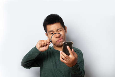 young man looking through magnifying glass at smartphone on gray background.の写真素材