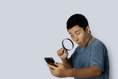 young man looking through magnifying glass at smartphone on gray background.の写真素材