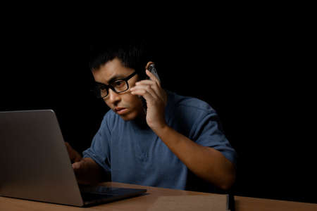 Young man with eye glasses using a smartphone and computer laptop at home, work from home concept on...