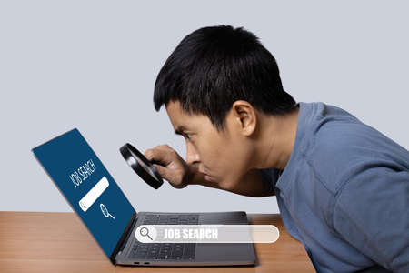 Young man observing laptop with magnifying glass to job search. job search concept.の写真素材