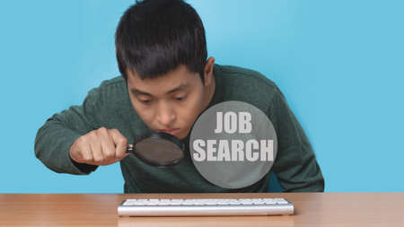 Young man using online computer keyboard with magnifying glass to job search. job search concept.の写真素材