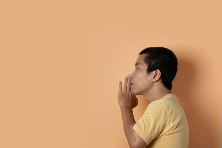 Young man whispering a secret behind hand isolated on orange studio background. Secret, gossip concept.の写真素材