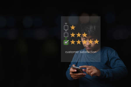 Asian man using smartphone with virtual screen on the smiley face icon on the digital touch screen. Customer service evaluation concept.の写真素材