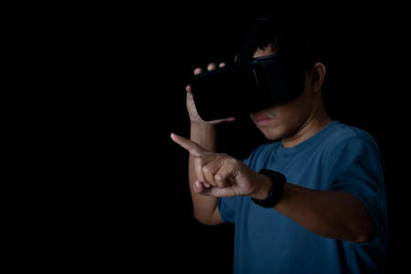 Studio portrait man wearing VR Headset touching something by his fingers on black background....