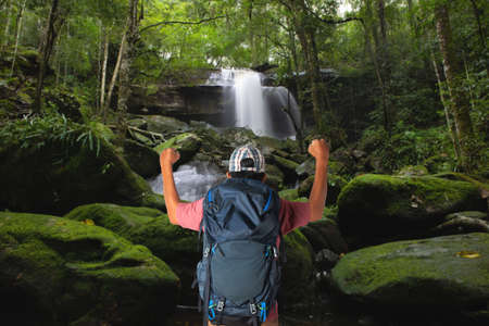 Young man with backpack enjoying waterfall in forest. Tourist traveler on background beautiful waterfall landscape.の写真素材