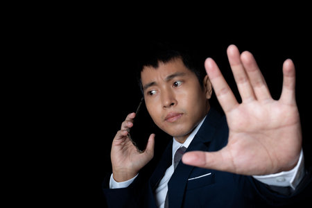 Portrait of businessman using smartphone show stop gesture sign by hand. Human emotion face expression concept. Studio shot on black background. copy space.の写真素材