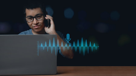 Young man using computer laptop and talking smartphone using voice assistant talking to smartphone for access to information. Virtual assistant App.の写真素材