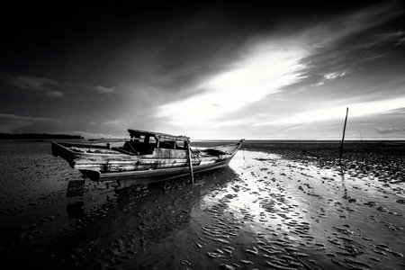 Black and white image of boat on the beach at sunset.の写真素材