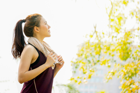 Asian sport woman with towel running / jogging in park on yellow flower backgroundの写真素材