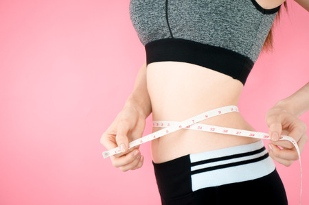 Asian beauty woman in sport bra showing fit body with tape measure on pink background for advertisementの写真素材
