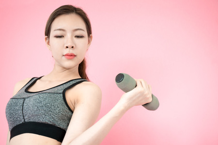 Asian beauty woman in sport bar exercise by lifting dumbbell on pink backgroundの写真素材