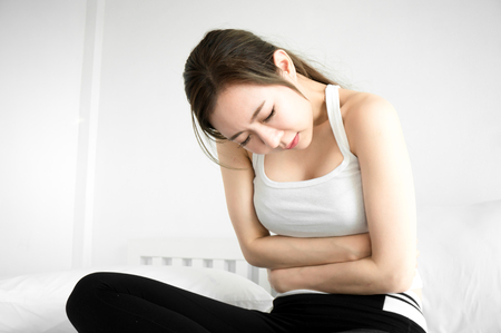 Asian beauty woman have a stomachache on white bed in white bedroom in morningの写真素材