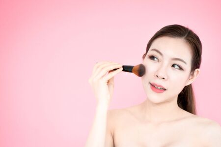 Asian beauty woman with blush brush present product for face on pink backgroundの写真素材