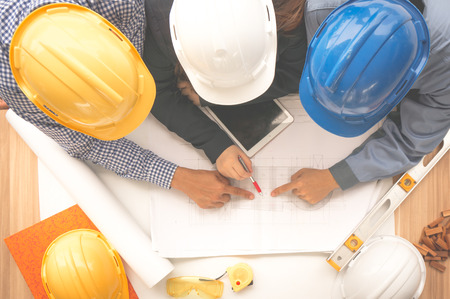Engineer and foreman wearing safety helmet are meeting at site outdoor and pointing to drawing paper top viewの写真素材