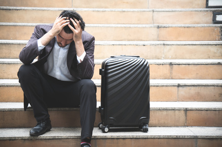 Business stress and sitting on stair with baggage in city outdoorの写真素材