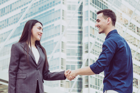 Businessman and woman shake hand on building in city backgroundの写真素材