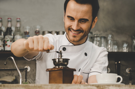 Barista grinding coffee bean and preparing hot coffee in coffee shop with smileの写真素材