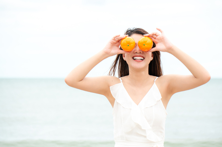 Asian woman with happy face and smile in summer on beach with orangesの写真素材