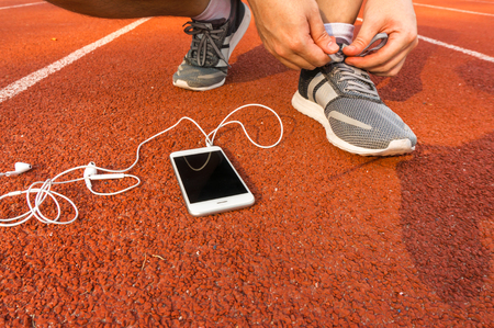 Asian sport man lace shoelace on racetrack with phone and headphonesの写真素材