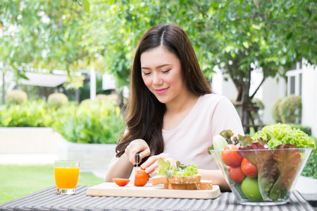Asian woman cut tomato for making sandwichの写真素材
