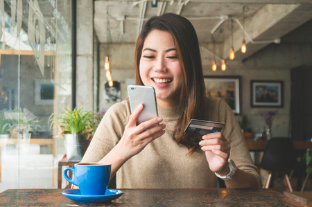 Asian woman shopping online with credit card payment in coffee shop feeling happy smileの写真素材