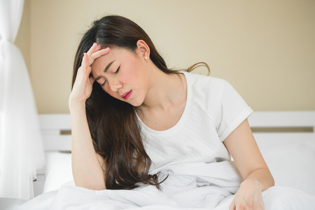Asian woman have a headache in bedroom morning because sleep problemの写真素材