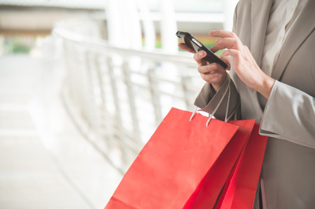 Asian woman holding shopping bag and chat via phone on walking way in the cityの写真素材