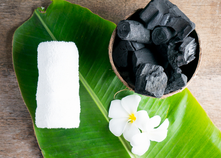 charcoal in coconut shell for spa on the wood background with white towel and flower on banana leaf for advertisementの写真素材