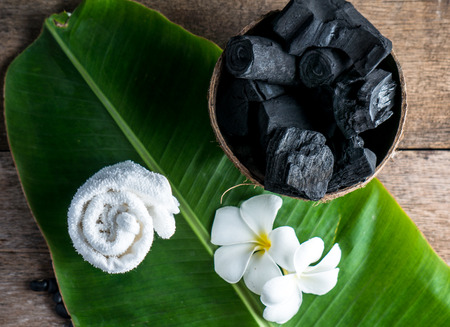 charcoal in coconut shell for spa on the wood background with white towel and flower on banana leaf for advertisementの写真素材