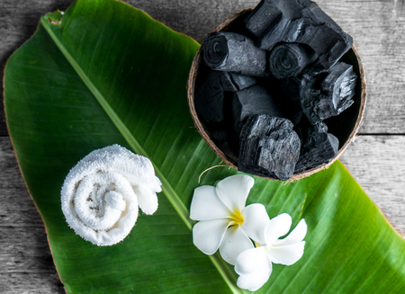charcoal in coconut shell for spa on the wood background with white towel and flower on banana leaf for advertisementの写真素材