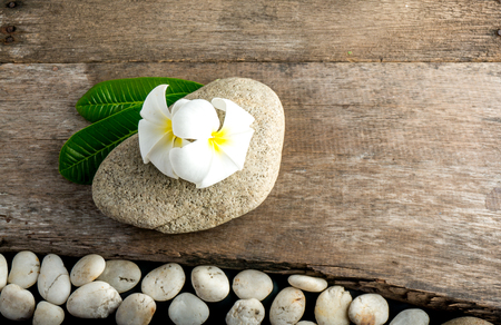White flower and leafs with big and tiny stone and towel on wood table for health spa advertisement and presentationの写真素材