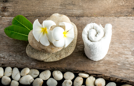 White flower and leafs with big and tiny stone and towel on wood table for health spa advertisement and presentationの写真素材