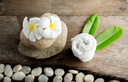 White flower and leafs with big and tiny stone and towel on wood table for health spa advertisement and presentationの写真素材