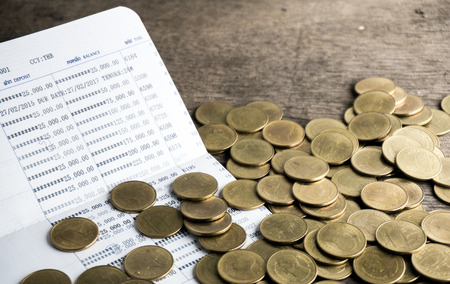 Saving money with gold coin stack and book bank on wood table for investment, business and advertisementの写真素材
