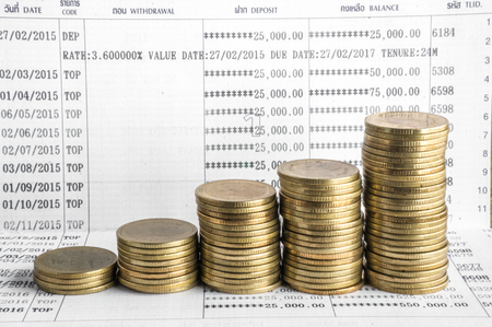 Saving money with gold coin stack and book bank on wood table for investment, business and advertisementの写真素材